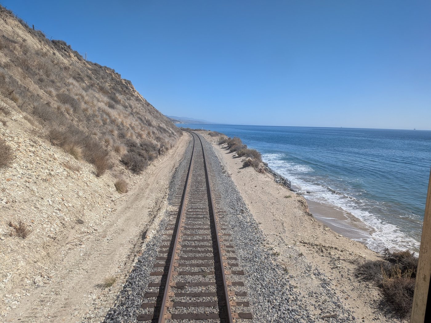 Train tracks running along the Pacific under a dry hillside